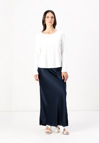 White long-sleeve top with textured fabric paired with a smooth navy satin maxi skirt, featuring a relaxed fit and subtle sheen.
