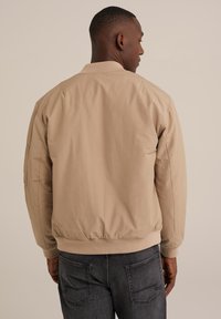 Béžová bomber bunda s žebrovaným límcem a manžetami, s hladkou texturou, elastickým spodním lemem a bočními kapsami, zobrazená zezadu.