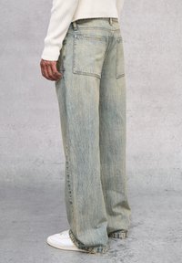 Jean de mezclilla en azul claro con corte holgado, con una textura deslavada y dos bolsillos traseros, combinados con zapatillas blancas.