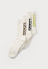 Trois chaussettes blanches en mélange de coton, chacune arborant un logo coloré : marron, noir et vert lime, avec des poignets côtelés pour l'élasticité.