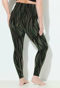 Leggings avec une base noire texturée présentant des motifs ondulés verts et dorés métalliques, un matériau extensible et une taille haute.