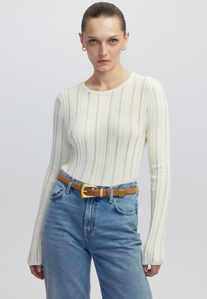Witte ribbelige langekthrough t-shirt met een ronde hals, gecombineerd met lichtblauwe high-waisted jeans en een bruine riem met een gouden gesp.