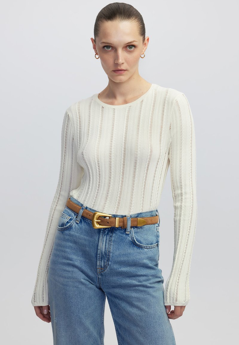 Weißes geripptes Langarmoberteil mit rundem Ausschnitt, kombiniert mit hellblauen hochgeschnittenen Jeans und einem braunen Gürtel mit goldener Schnalle.
