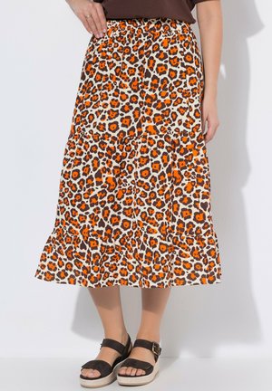 Mujer con falda midi de estampado de leopardo en tonos naranja y marrón, y sandalias negras de plataforma, sobre un fondo blanco.