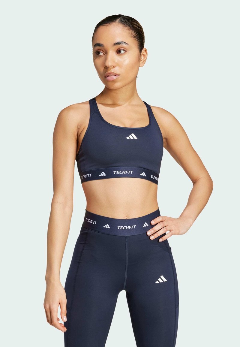 Marineblauwe sportbeha met brede banden en logo. Bijpassende high-waisted leggings met een elastische band en logo op de taille en dij.