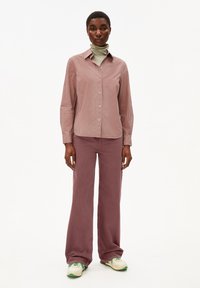 Camicia a maniche lunghe a righe in morbido tessuto rosa, abbinata a pantaloni larghi viola. Indossata con un dolcevita verde chiaro e sneaker.