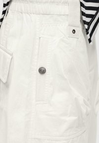 Λευκή cargo φούστα με κούμπωμα με κουμπιά τύπου snap, μπροστινές τσέπες και ένα μαύρο-λευκό ριγέ τοπ μέσα στη φούστα.