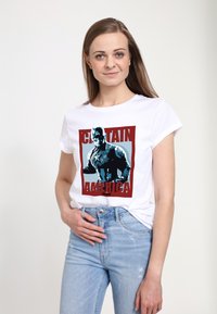Biały T-shirt z grafiką Kapitana Ameryki w niebiesko-czerwonych kolorach, z krótkimi rękawami, okrągłym dekoltem i swobodnym krojem, w połączeniu z jasnoniebieskimi dżinsami.