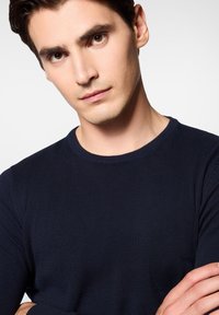 Granatowy sweter dzianinowy z okrągłym dekoltem. Gładka faktura, dopasowany krój i widoczne szwy wzdłuż brzegów.