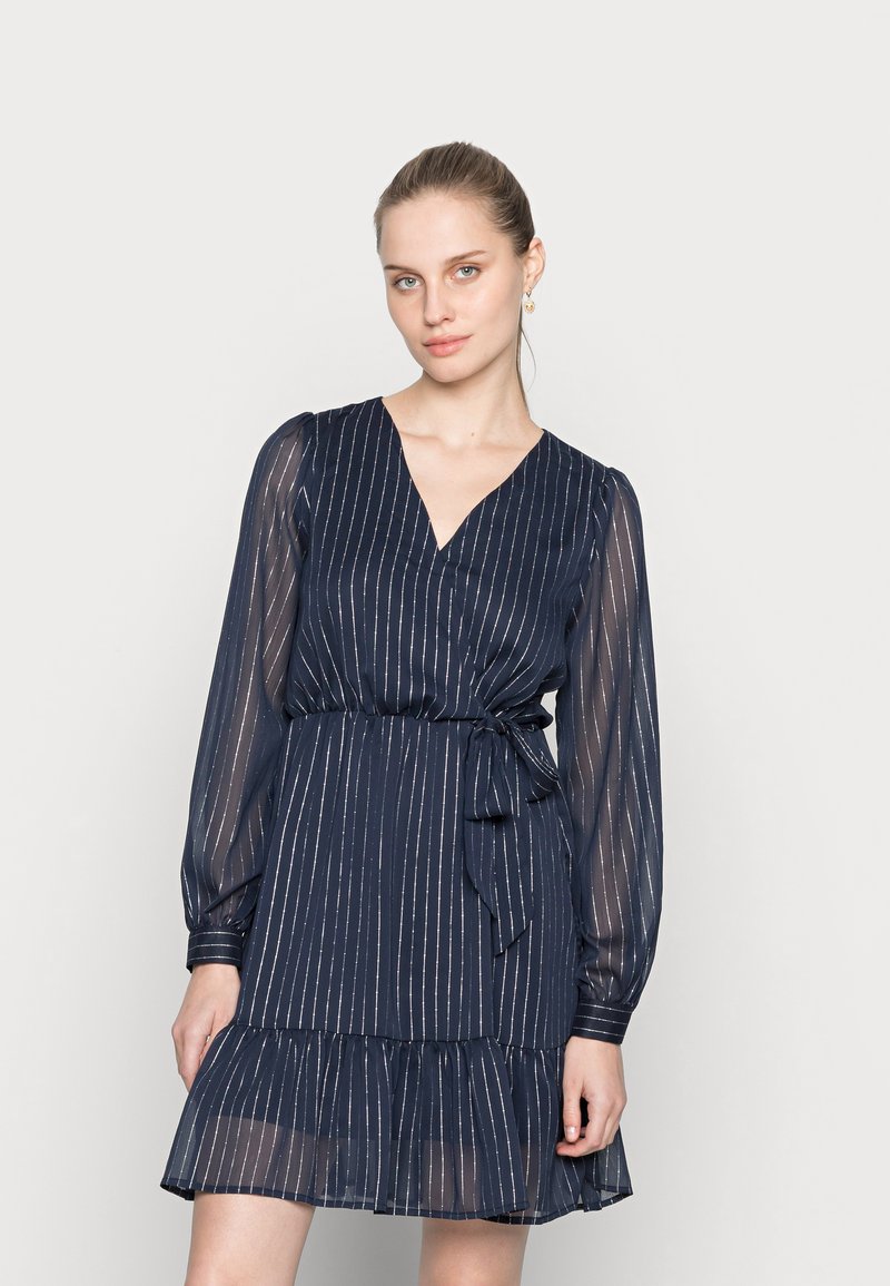 Vestido azul marinho com mangas longas transparentes, decote em V e cintura ajustada. Apresenta uma barra em camadas com babados e listras verticais subtis.