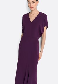 Paarse jurk van gladde stof, met een diepe V-hals, korte mouwen en een getailleerd silhouet met een split aan de zoom.