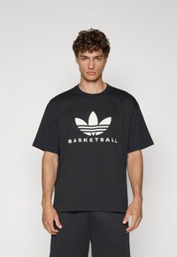 Svart bomulls t-shirt med korta ärmar och rund halsringning, med en vit "BASKETBALL"-tryck och en stiliserad logotyp på framsidan.