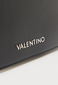 Superficie in pelle nera texturizzata con logo metallico argentato "VALENTINO" centrato vicino al bordo inferiore.