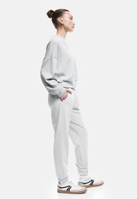 Lichtgrijze sweatshirt met een relaxed fit, met manchetten aan de mouwen, gecombineerd met bijpassende joggers en witte sneakers met zwarte accenten.