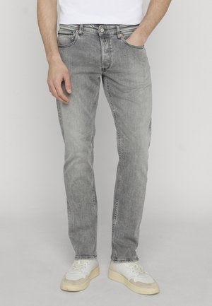 Mand iført lysegrå falmede jeans, den ene hånd i lommen, kombineret med hvide sneakers mod ensfarvet baggrund.