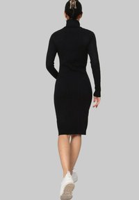 Robe en tricot côtelé noir avec un col haut et des manches longues, longueur genoux, associée à des baskets blanches. Design et texture minimalistes.