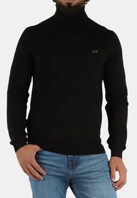 Maglione a collo alto nero in un tessuto elastico, caratterizzato da una vestibilità slim e un piccolo logo verde sul lato sinistro del petto. Maniche lunghe con polsini a costine.