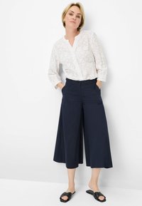 White, embroidered shirt with three-quarter sleeves, paired with navy wide-leg pants. Black slide sandals complete the outfit.