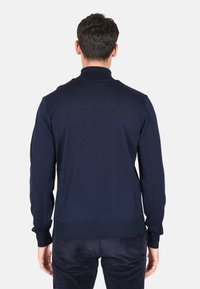 Maglione lavorato a maglia blu navy con maniche lunghe, colletto alto e polsini e orlo a costine. Texture liscia, design aderente. Vista posteriore mostrata.