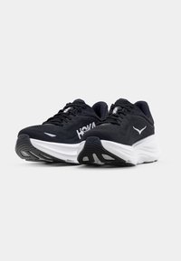 Chaussures de course noires avec tige en mesh, semelle intermédiaire blanche, semelle texturée et logo HOKA. Comprend des lacets et un col rembourré pour un soutien.