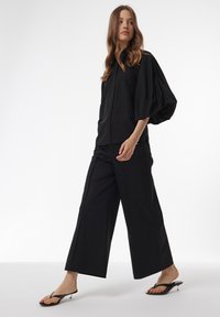 Zwarte blouse met poffende mouwen, gecombineerd met brede zwarte broek en zwarte slippers. Soepele textuur en casual ontwerp.