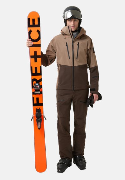 Snowboard met een feloranje basis en zwarte tekst. De bestuurder is uitgerust met een bruine en grijze jas, bijpassende bruine broek en handschoenen.