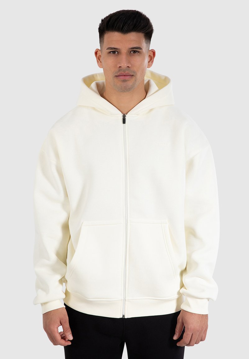 Vit zip-up hoodie tillverkad av mjukt material. Har en huva med dragsko och framfickor. Ribbad mudd och nederkant ökar komforten.