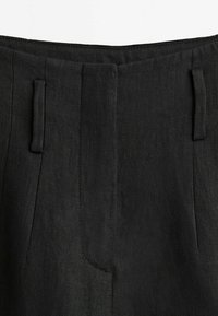 Gros plan sur la ceinture d'un pantalon noir avec passants pour ceinture et fermeture éclair avant dissimulée.