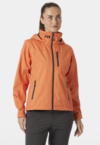 Oranje waterdichte jas met capuchon, rits aan de voorkant en twee zijzakken. Voorzien van zwarte ritsen en logo op de kraag. Soepele textuur.