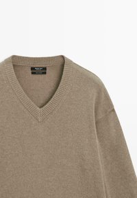 V-Ausschnitt-Pullover aus hellbeigem Strick mit geripptem Kragen und Bündchen, der eine weiche Textur und eine lässige Passform aufweist. Logotag im Halsbereich sichtbar.