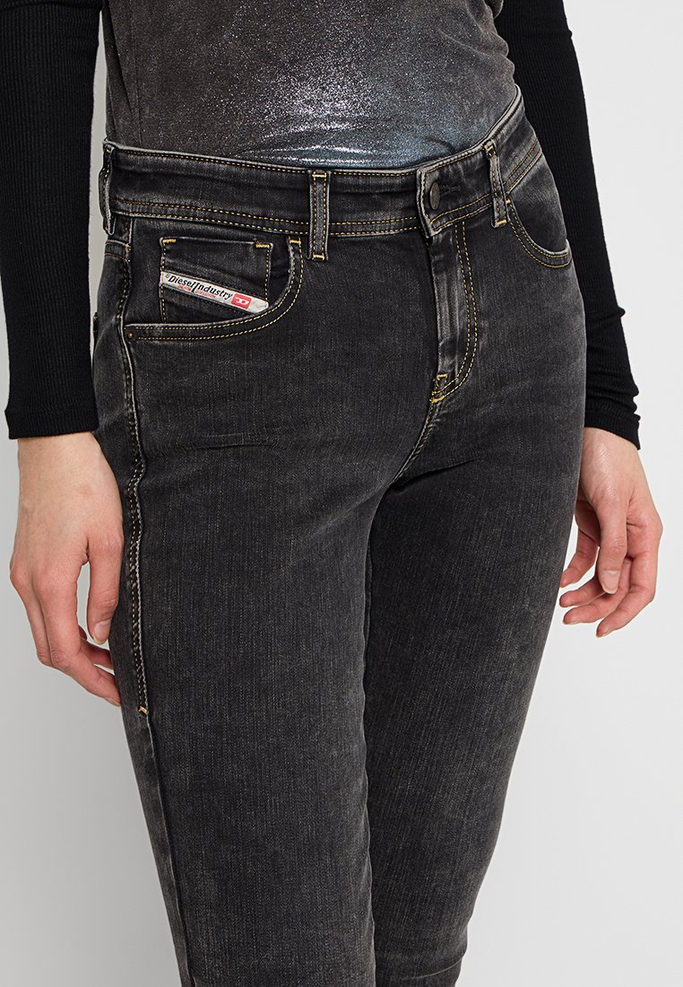 Persona che indossa jeans in denim nero lavati e una maglietta nera a maniche lunghe, con una camicia metallica argento parzialmente visibile.