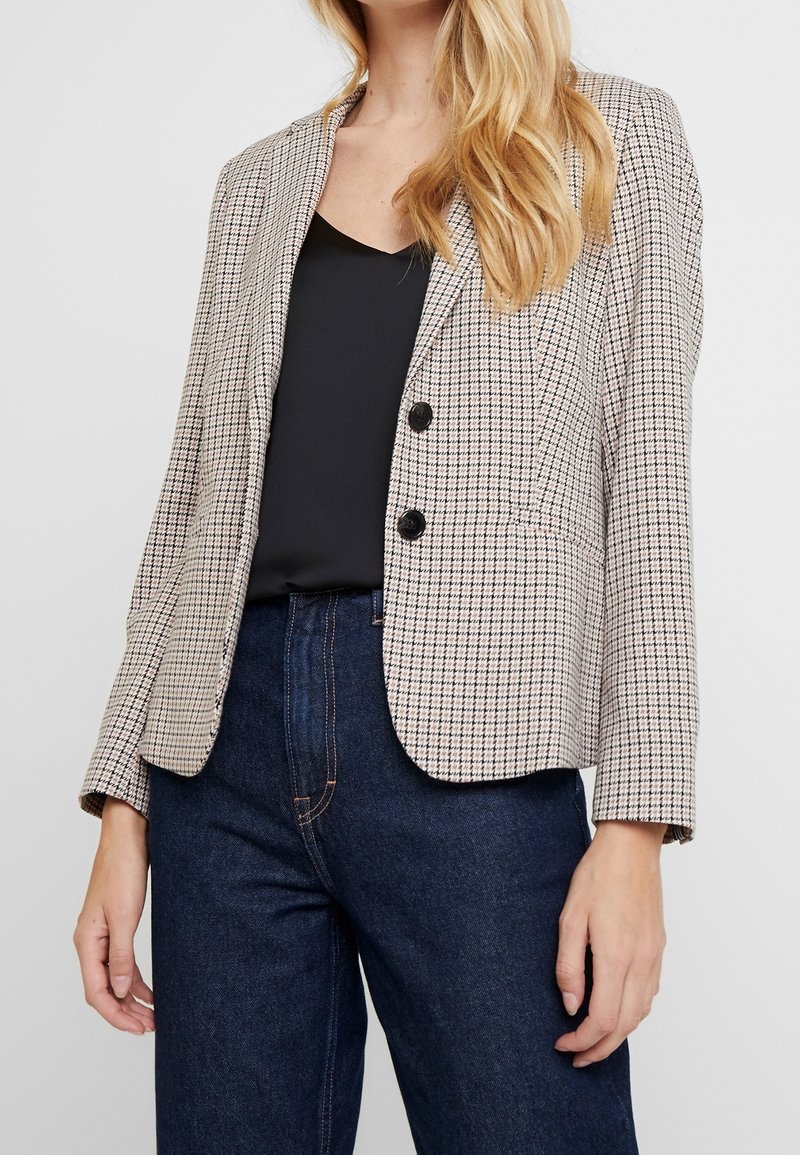 Karmelowy żakiet w beżowo-czarnym kolorze, dopasowany krój, jednorzędowy z dwoma guzikami, z klapami oraz dwiema przednimi kieszeniami.