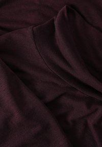 Bordó szövet sima textúrával. Lazán álló nyakvonal jellemzi, puha redők, és finom varrási részletek láthatók a széleken.