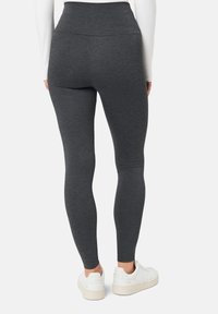 Szare leginsy z wysokim stanem wykonane z rozciągliwej tkaniny, o gładkiej fakturze i dopasowanym kroju. Noszone z białymi butami sportowymi.