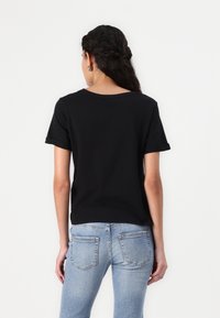 Black short-sleeve t-shirt with a relaxed fit, round neckline, and rolled sleeves. Paired with light blue denim jeans.