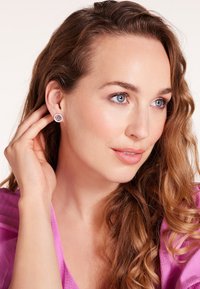 Zilveren oorbellen met een cirkelontwerp, gekenmerkt door een centrale edelsteen en intricaat detailwerk. Model toont de oorbellen terwijl ze haar haar aanraakt.