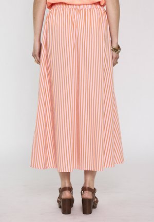 Femme portant une jupe midi rayée verticale rose et orange, des sandales marron à talons et des bracelets dorés, vue de dos.