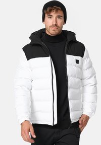 Puffjakke med hvid krop og sort skulderpanel, der har en lynlås, elastiske manchetter og en foret hætte til isolering.