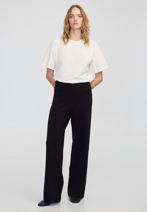 Witte t-shirt met korte mouwen, gecombineerd met zwarte hoge taille wijde broek. Glad materiaal, relaxte pasvorm, minimalistisch ontwerp.