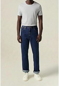 Vaqueros de mezclilla azul oscuro con puños remangados, que cuentan con cinco bolsillos, costuras cosidas y una camiseta gris ajustada de cuello redondo. Zapatillas blancas completan el conjunto.