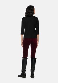 Schwarzes Oberteil mit Dreiviertelärmeln, burgunderfarbene Cordhosen und knielange schwarze Lederstiefel mit einem kräftigen Absatz, von hinten gesehen.
