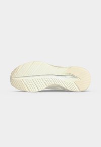 Semelle d'une chaussure de sport blanche avec des rainures diagonales et verticales pour l'adhérence, présentée sur un fond clair uni.