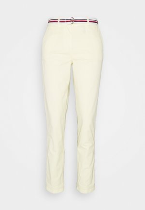 Jasnożółte spodnie o dopasowanym kroju i podwiniętych mankietach, z paskiem w paski w odcieniach czerwieni i granatu. Gładka tekstura tkaniny.