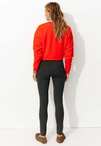 Sweat-shirt rouge vif à coupe ample, associé à des leggings gris foncé et des ballerines à imprimé léopard. Texture lisse, design décontracté.