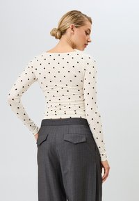 Langermige, aansluitende top in crèmekleur met zwarte stippen, gecombineerd met grijze pinstripe broeken met achterzakken en een getailleerde pasvorm.