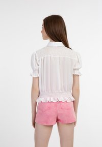 Weiße Bluse mit Puffärmeln, einem gesmokten Rücken und einem Rüschensaum, kombiniert mit rosa Jeansshorts mit dezenten Taschen und einer leicht verblassten Textur.