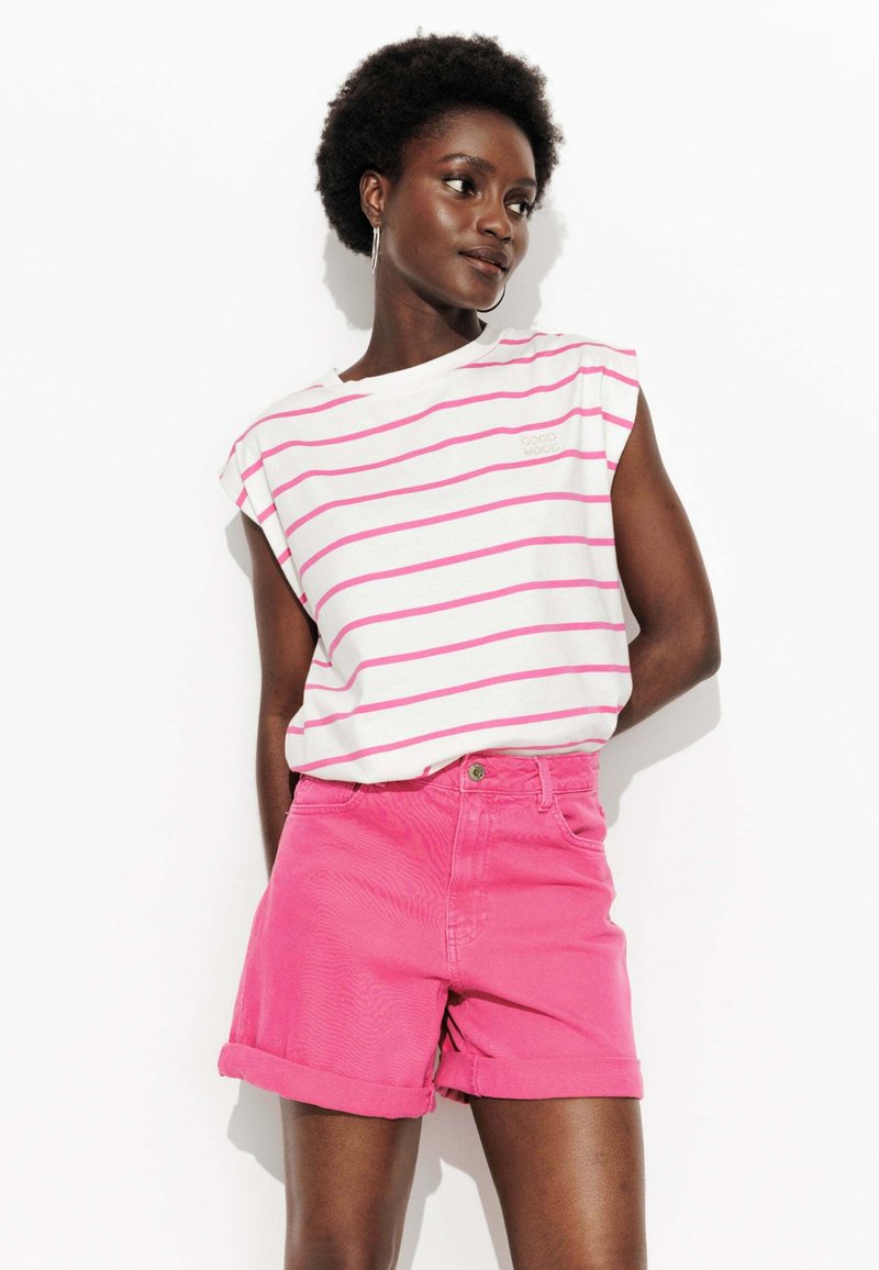 Chemise sans manches blanche avec des rayures roses, associée à un short rose taille haute. Les deux vêtements ont une coupe décontractée et une texture lisse.