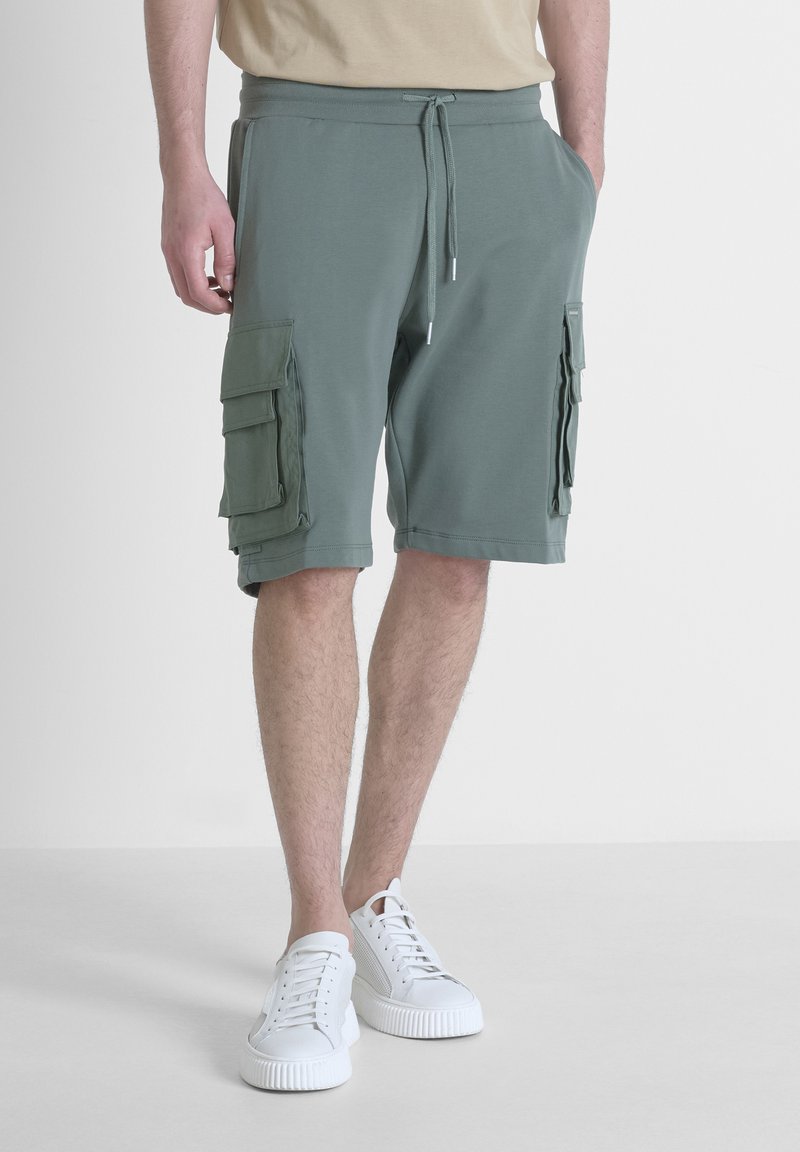 Groene cargoshorts van zacht materiaal; uitgerust met twee grote zijzakken met kleppen, een elastische tailleband en een trekkoordsluiting.