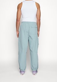 Ljusblå cargobyxor med elastisk midja, sidofickor och smalnade anklar, kombinerade med lila rutiga Vans-sneakers.