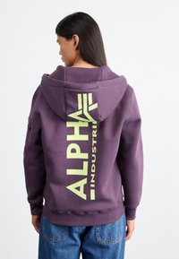 Felpa viola con grande stampa gialla "ALPHA INDUSTRIES" sul retro, dotata di cappuccio con cordino e polsini a costine.